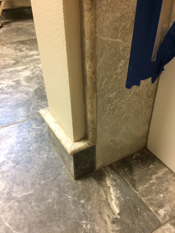 Close-up of a pillar with gray tile flooring. Beige and white sections with blue tape present.
