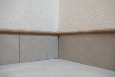 Corner of a room with light-colored tile baseboard, beige walls, and brown trim.