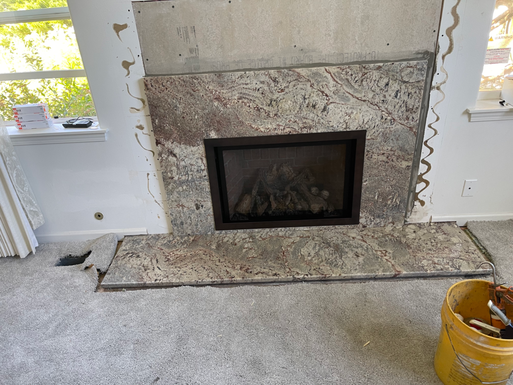 Fireplace with granite surround under renovation, exposed drywall and a bucket nearby.