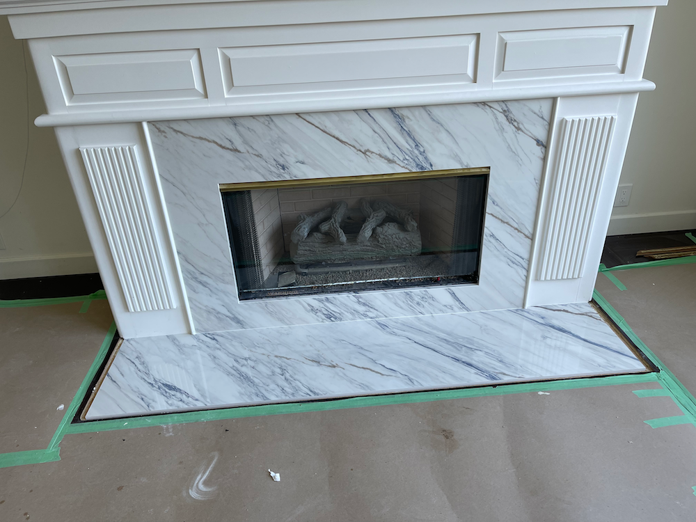 White marble fireplace with blue veining, set against a neutral wall; green tape outlines floor.