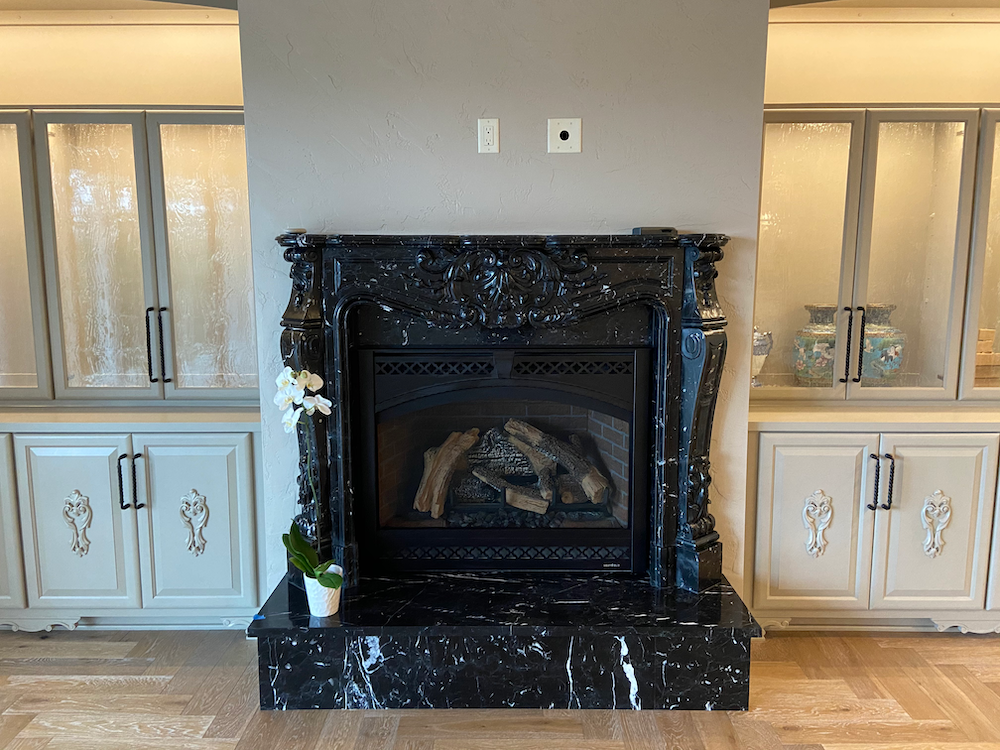 Black marble fireplace with carved details, flanked by cream and glass cabinets on a wood floor.