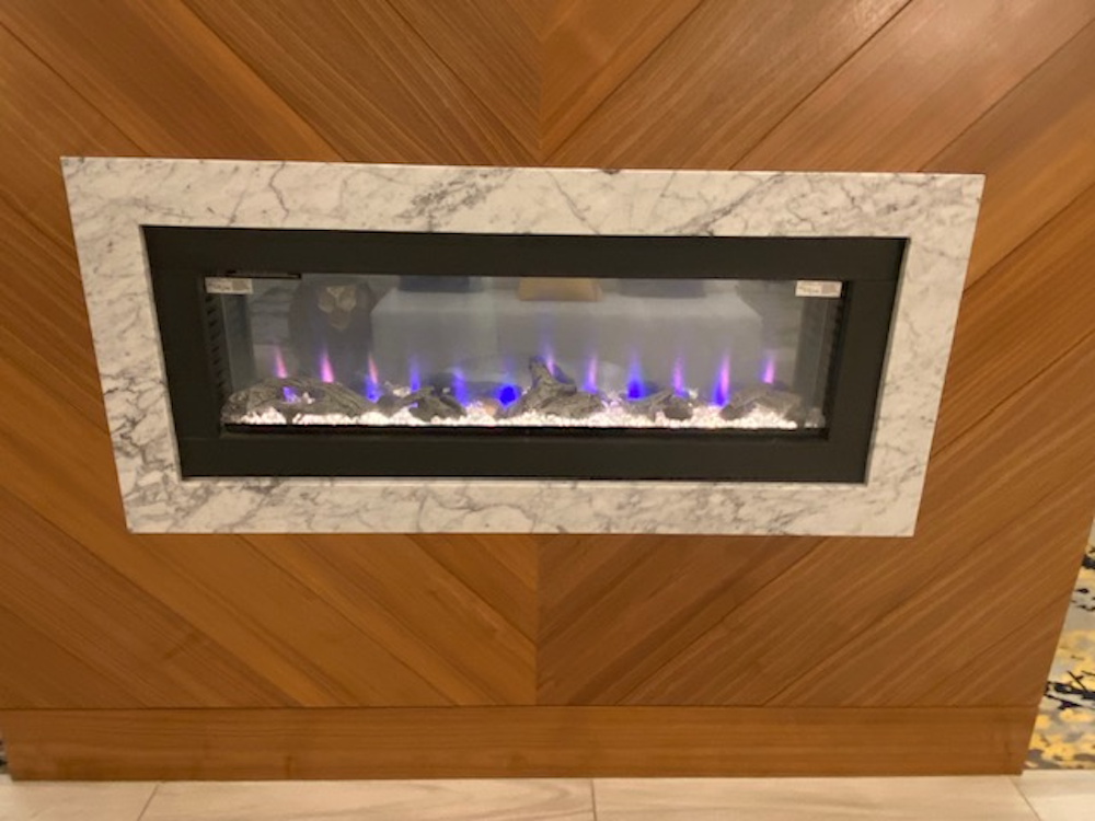 Electric fireplace with blue and purple flames, framed in marble, set in a wood-paneled wall.