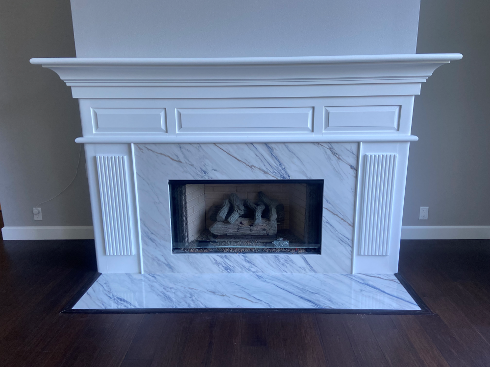 White fireplace with marble facing, dark wood floor, and gray walls.