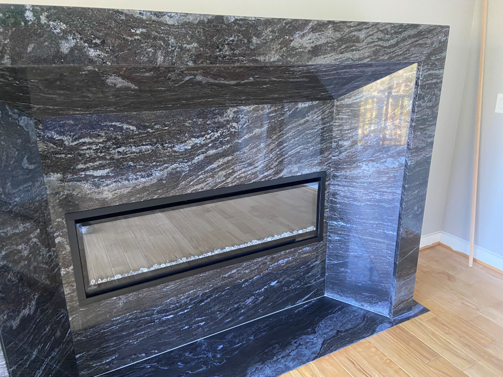 Black granite fireplace with a rectangular firebox, on a wooden floor.