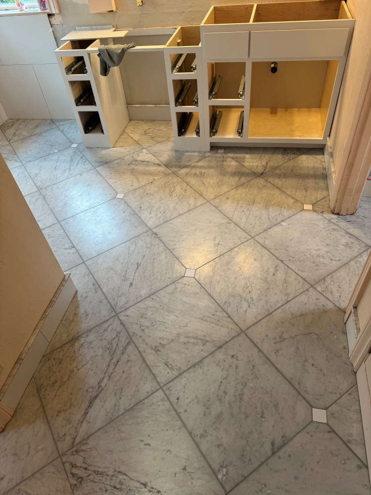 Kitchen floor with gray and white tile, unfinished cabinets.
