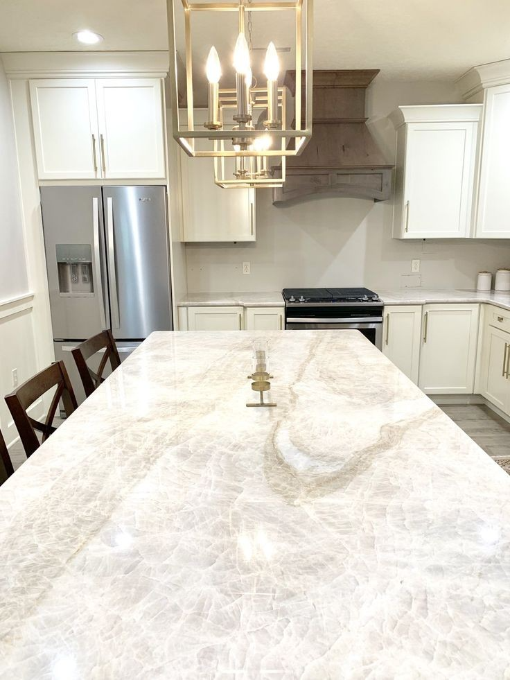 Elegant white kitchen with large island, gold chandelier, and stainless steel appliances.