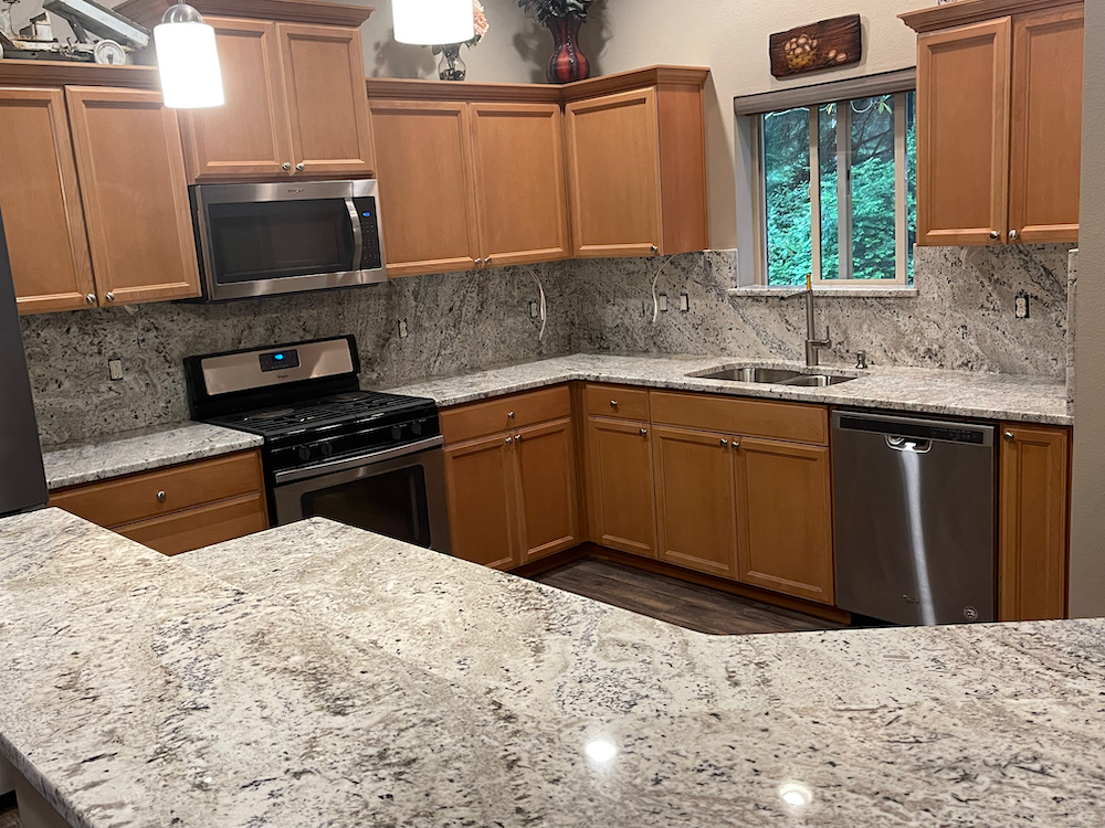 Kitchen with light wood cabinets, granite countertops, and stainless steel appliances.