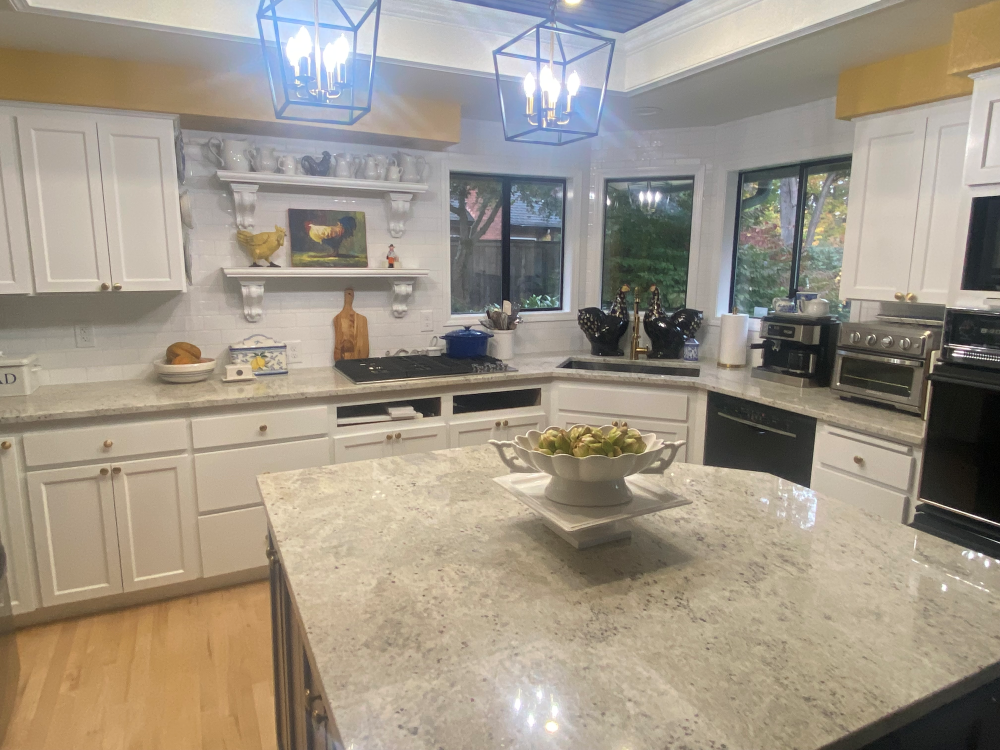 White kitchen with granite countertops, island, and cabinets. Includes stove, sink, and decorative shelf.