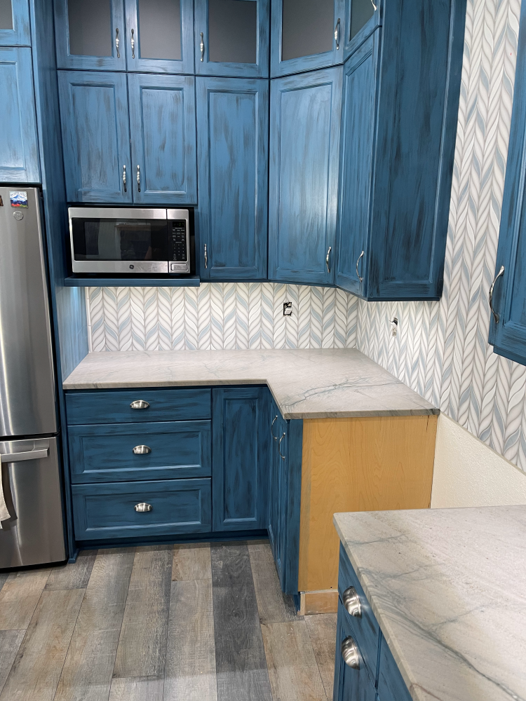 Blue kitchen cabinets with a stainless steel microwave and light countertops.