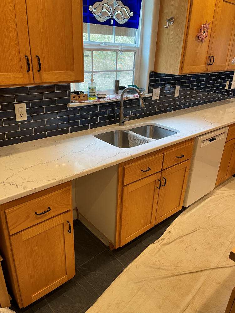 Kitchen with light wood cabinets, white countertops, and dark blue backsplash. Stainless steel sink.