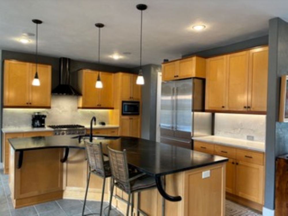 Modern kitchen with blonde wood cabinets, black countertops, and pendant lights.