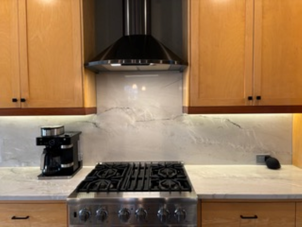 Kitchen with light wood cabinets, stainless steel stove, and marble backsplash.