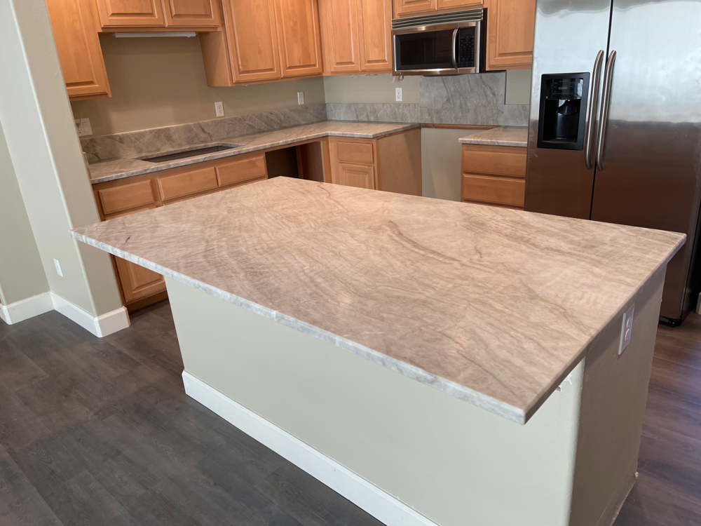 Kitchen with light wood cabinets, granite countertops, and an island. Dark flooring and stainless steel refrigerator.