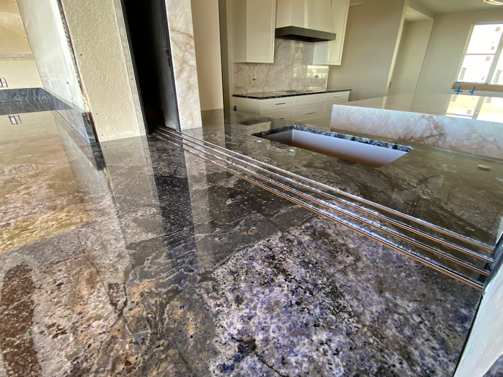 Close-up of a kitchen countertop and floor made of polished granite with various colors and textures.