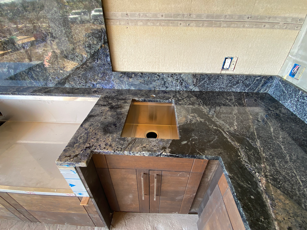 Granite countertop with a built-in sink and cabinets below. Dark gray stone, beige backsplash.