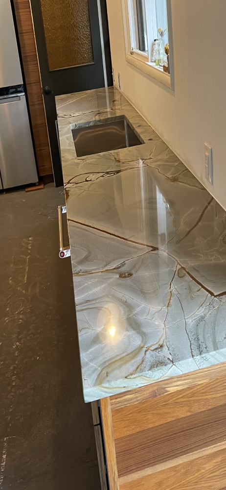 Kitchen counter with a marble countertop, wood cabinets, and a stainless steel sink.