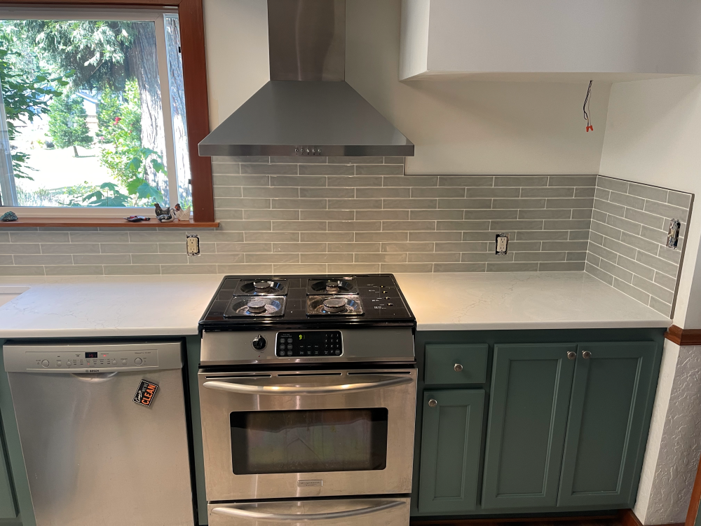 Kitchen with stainless steel appliances, green cabinets, gray backsplash, and white countertops.
