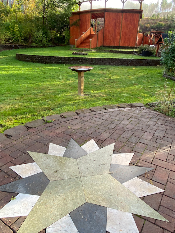 A backyard with a brick patio featuring a star design, a bird bath, and a wooden playhouse.