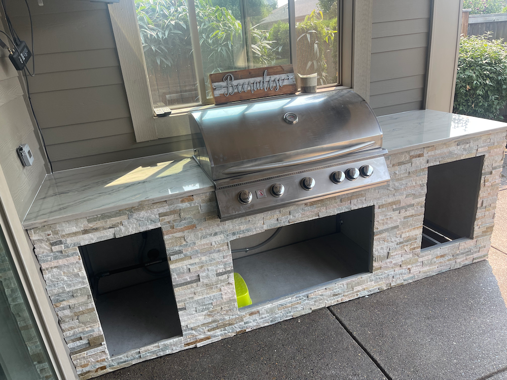 Outdoor kitchen with stainless steel grill, stone facade, and countertop.