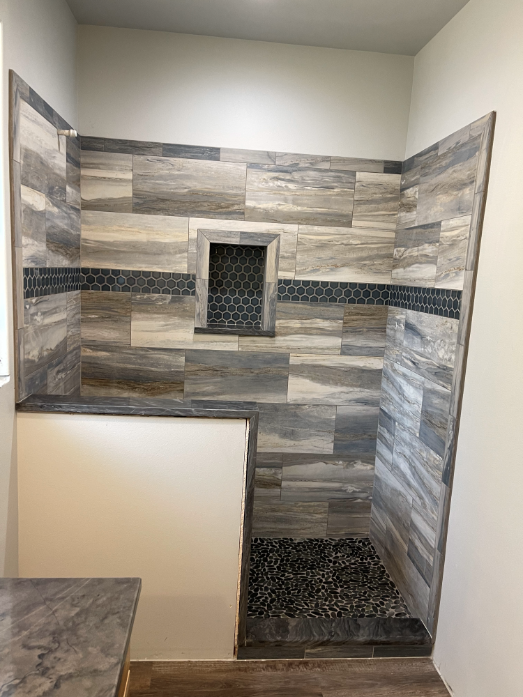 Shower with gray wood-look tile walls, pebble floor, and a dark tile band.