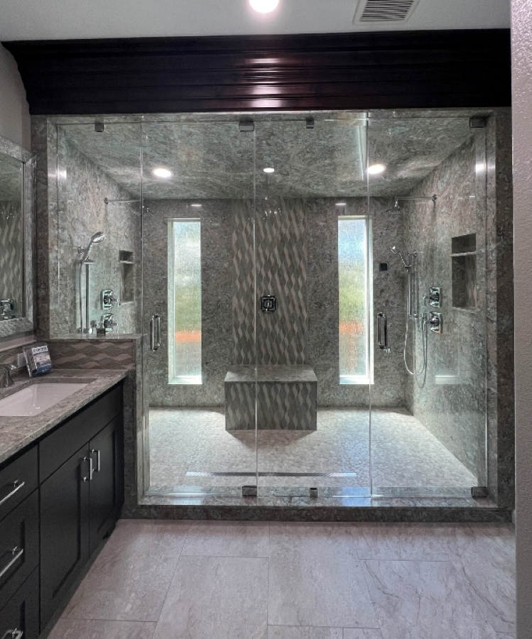 Luxurious bathroom with glass shower enclosure, gray marble tile, dark cabinetry, and a bench.