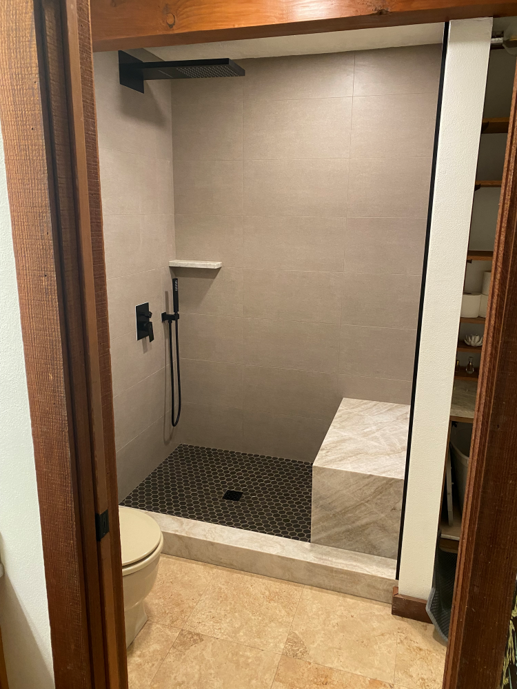Shower with gray tile walls, black fixtures, mosaic floor, and a stone bench.