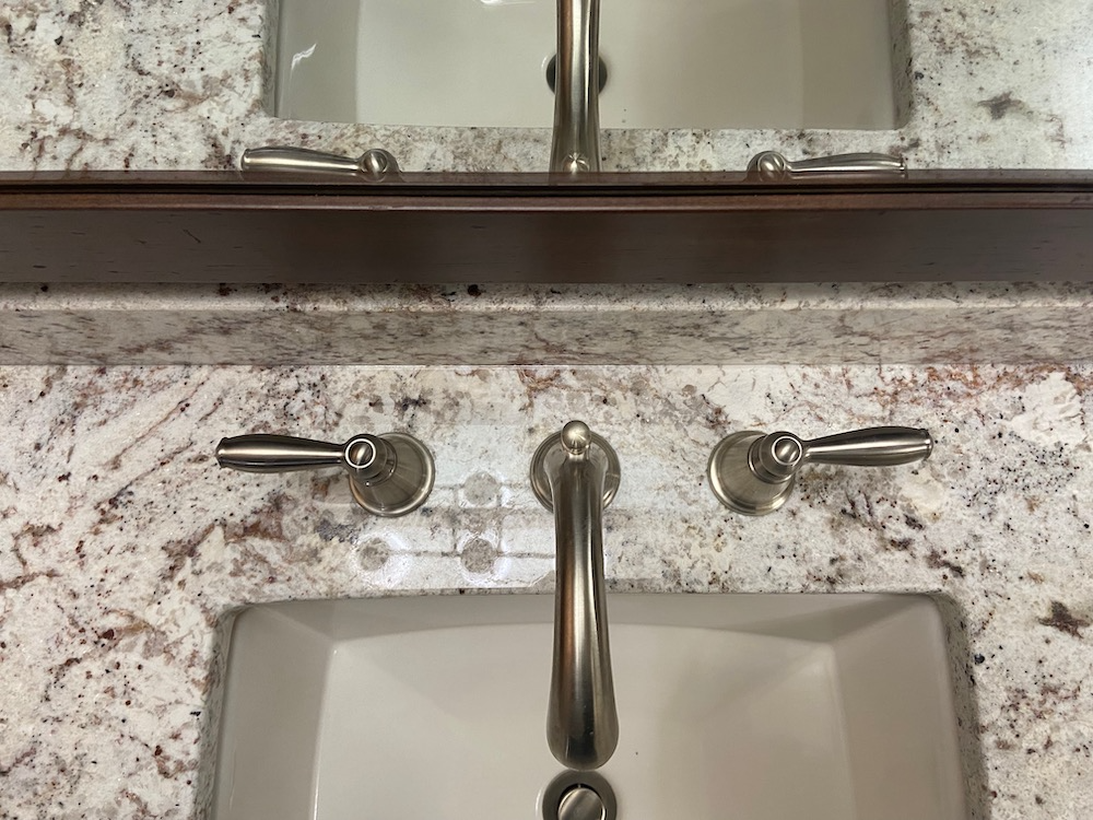 Bathroom sink with granite countertop and brushed nickel faucet and handles. Mirror above.