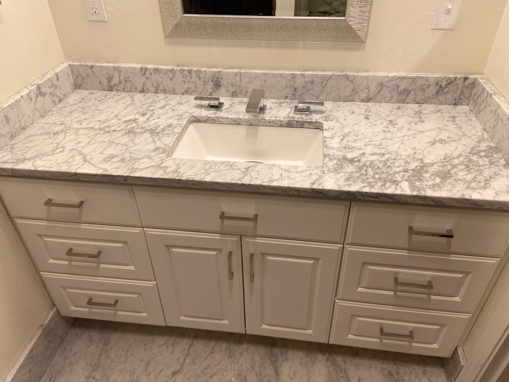 White bathroom vanity with marble countertop, rectangular sink, and chrome fixtures.
