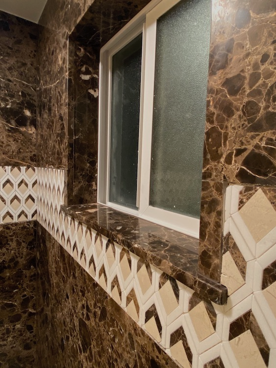 Bathroom with brown marbled walls, white window frame, and decorative tile border.