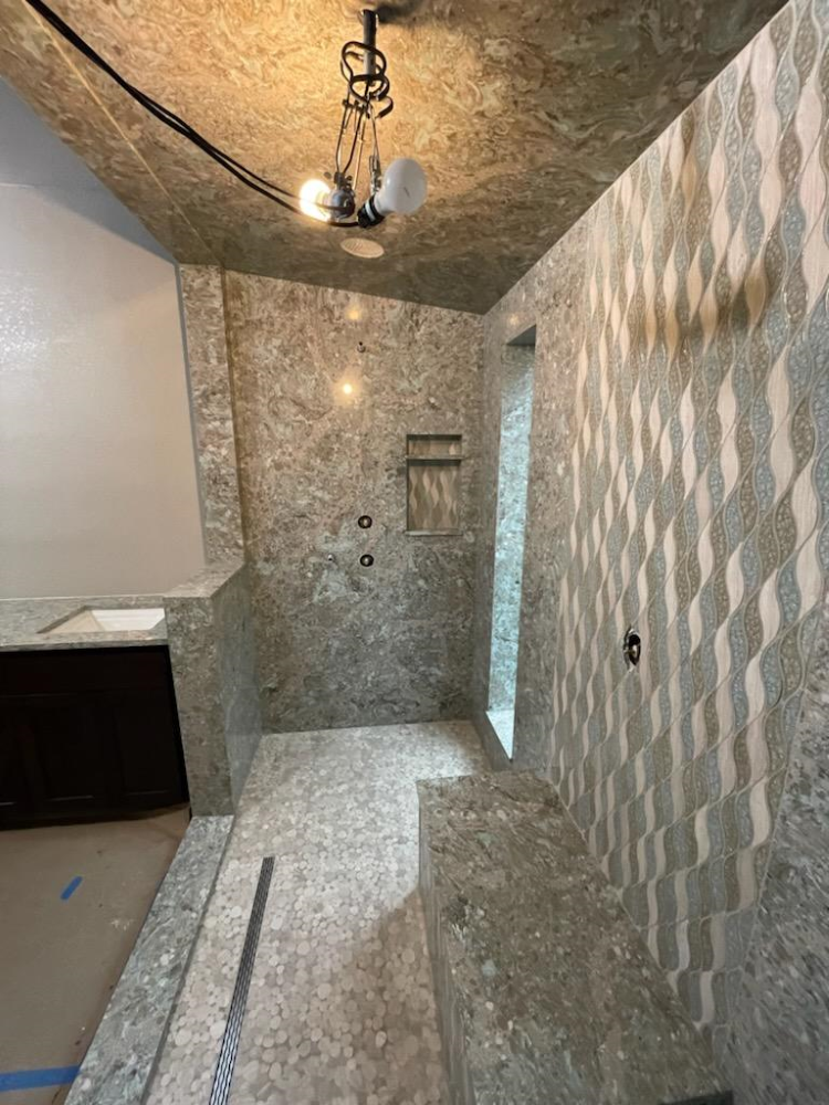 Finished shower with gray tiled walls and floor, built-in bench, and unique geometric pattern on one wall.