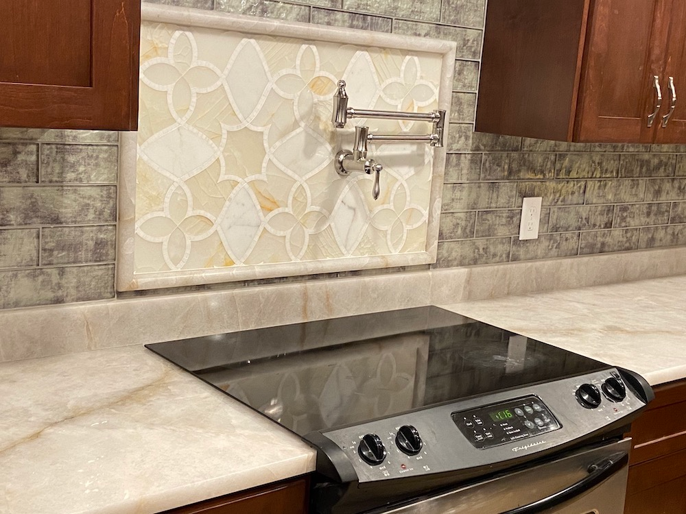 Kitchen with stovetop, backsplash, and pot filler. Countertops and cabinets are visible.