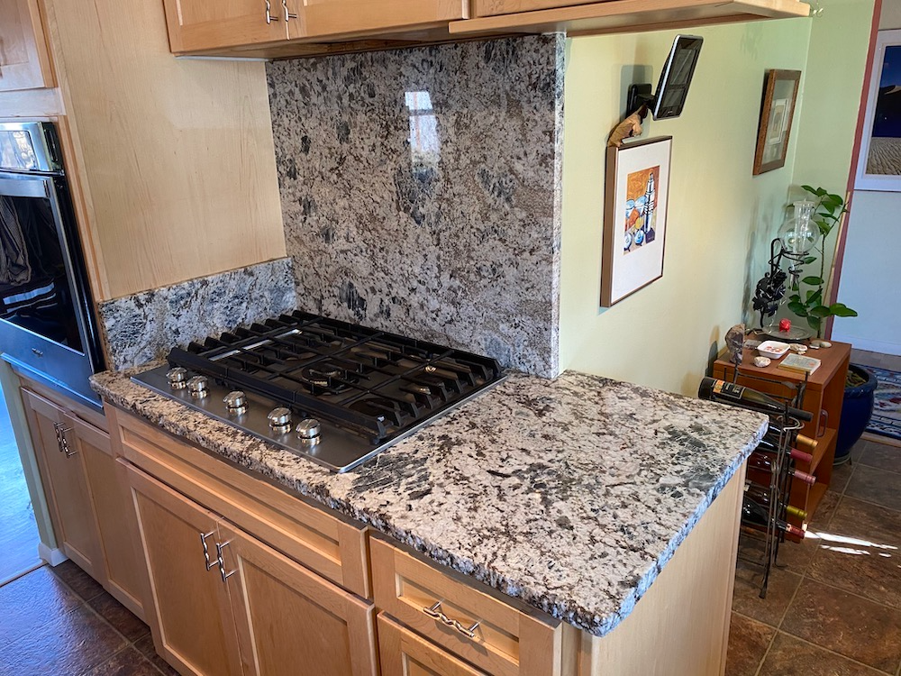 Kitchen with granite countertops and a stovetop. Light wood cabinets.