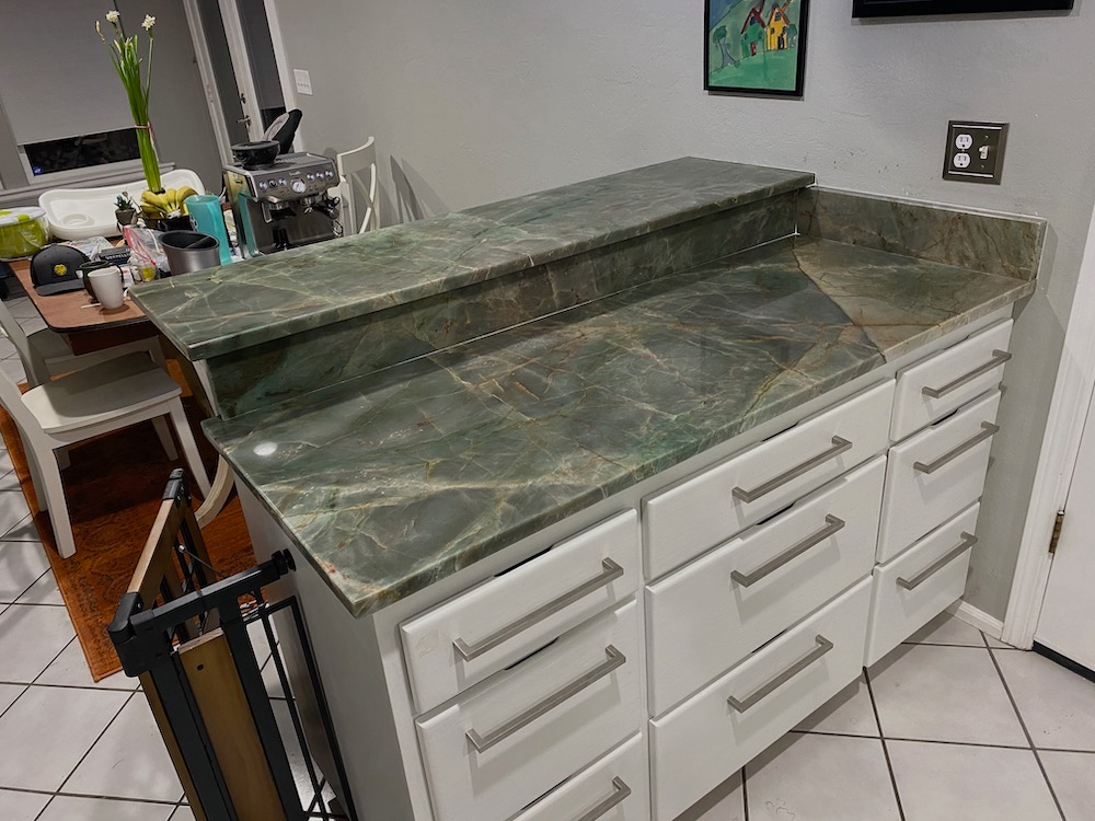 White cabinets with green marble countertop in a kitchen.