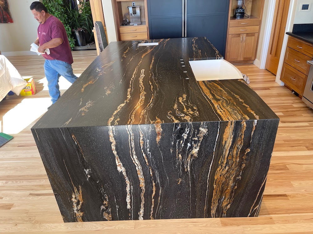 Kitchen island with black and gold patterned countertop, man in background.