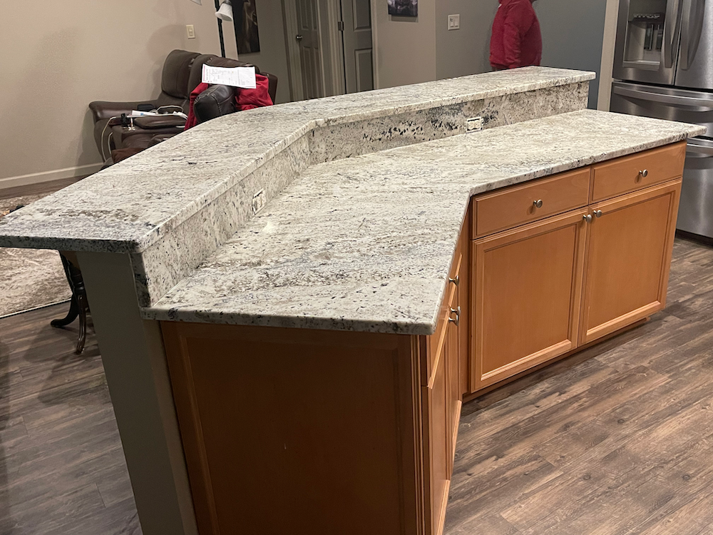 L-shaped kitchen island with light-colored granite countertop and wooden cabinets.