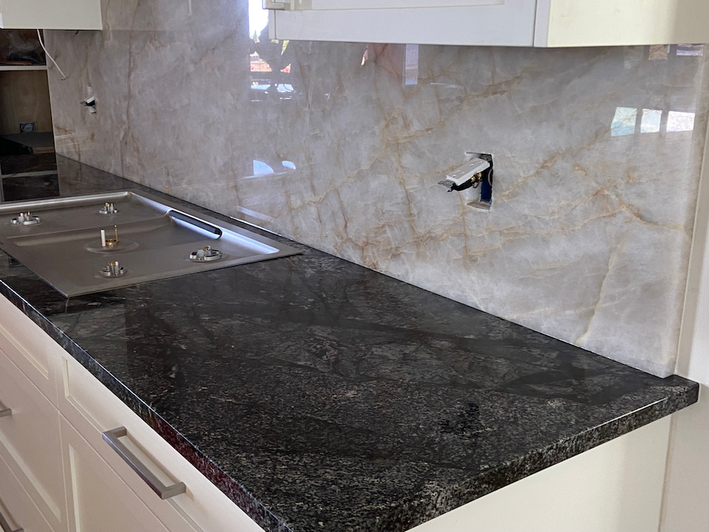 Kitchen with black granite countertop, light marble backsplash, and stainless steel sink.