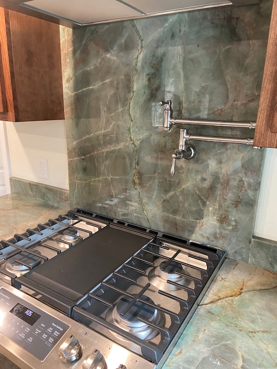 Gas stovetop with griddle and pot filler against a green marble backsplash and countertop.