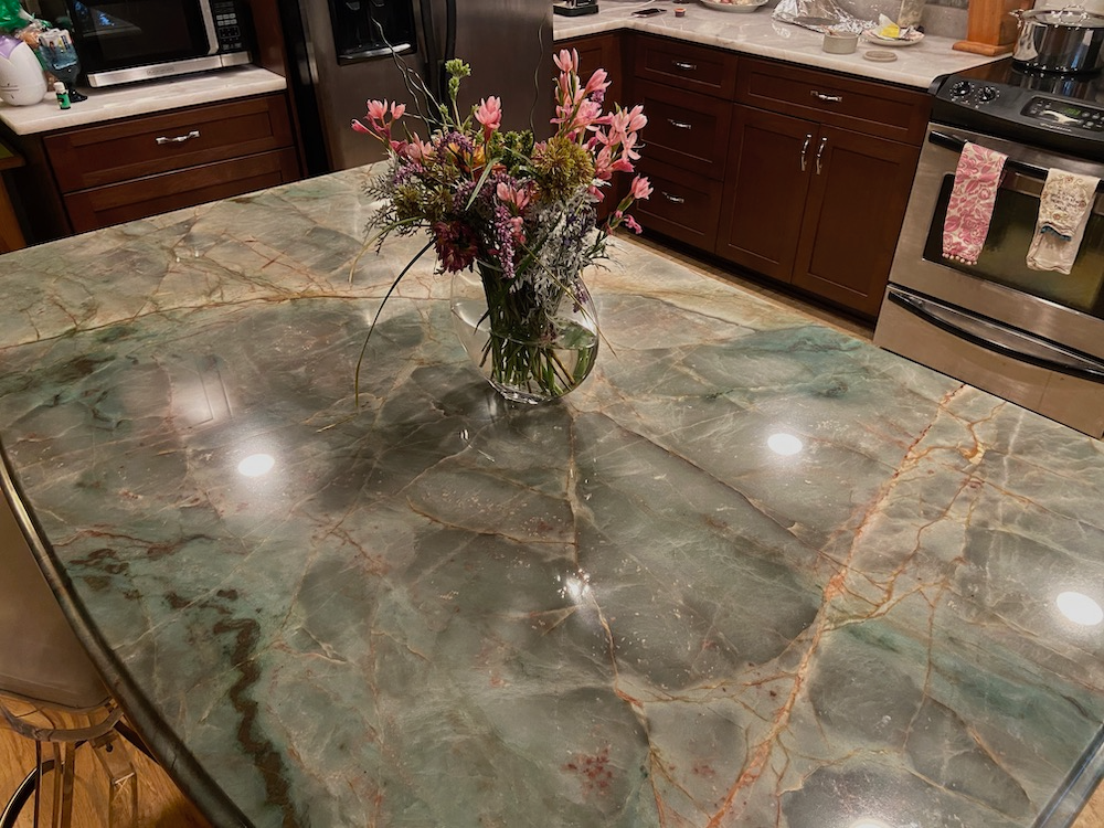 A kitchen with a large, green marble countertop, vase of flowers, and a stainless steel oven.