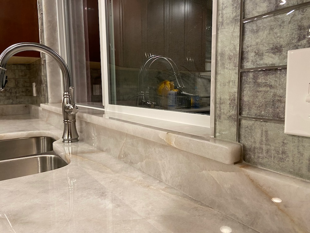 Kitchen countertop with a faucet, sink, and window overlooking another sink and cabinets.