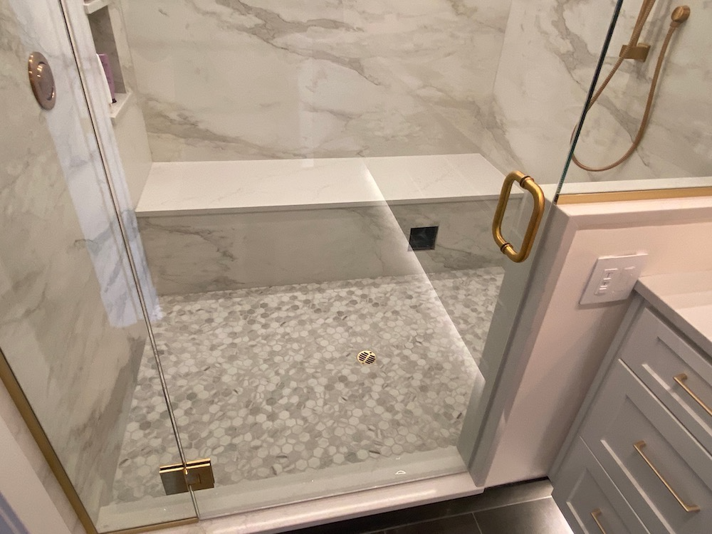 Modern shower with marble tile, pebble floor, glass door, and built-in bench.