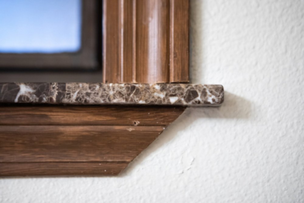 Close-up of a brown wooden window frame with a marble shelf against a white wall.