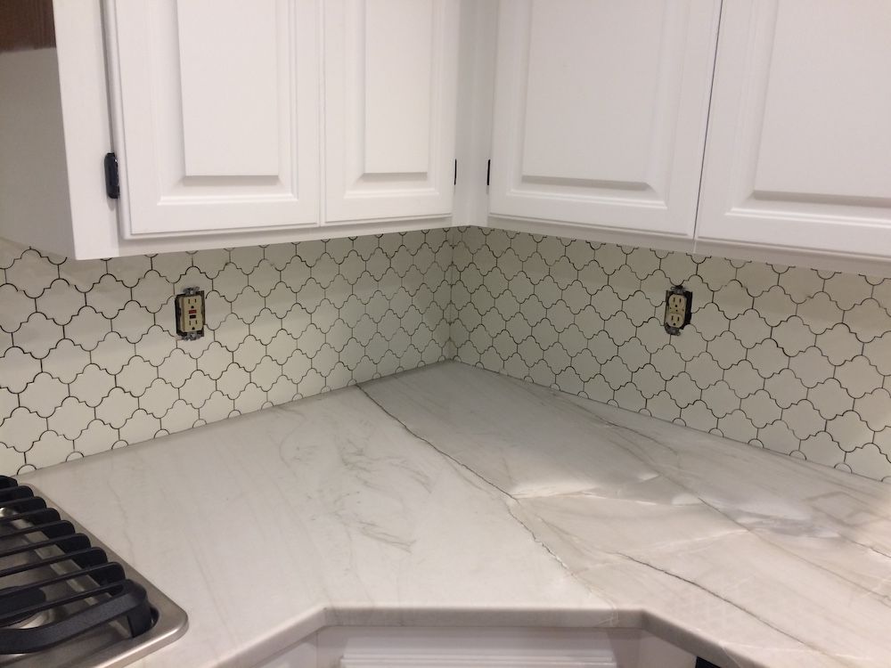 White kitchen cabinets with white patterned backsplash and light gray countertops.