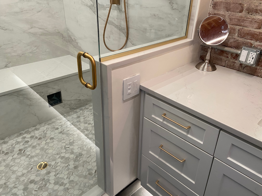 Bathroom with gray vanity, glass shower, and exposed brick wall.