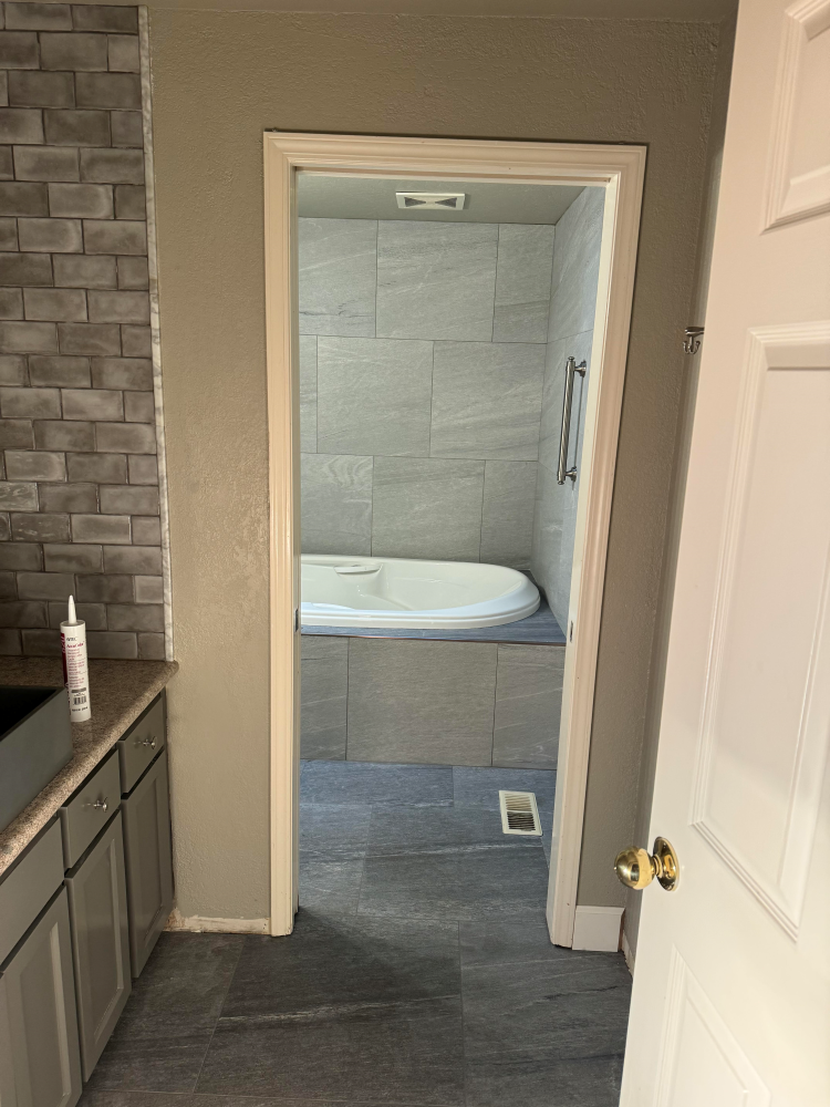 Bathroom doorway with a tile-surrounded bathtub. Gray walls, floor, and cabinetry; white door and trim.