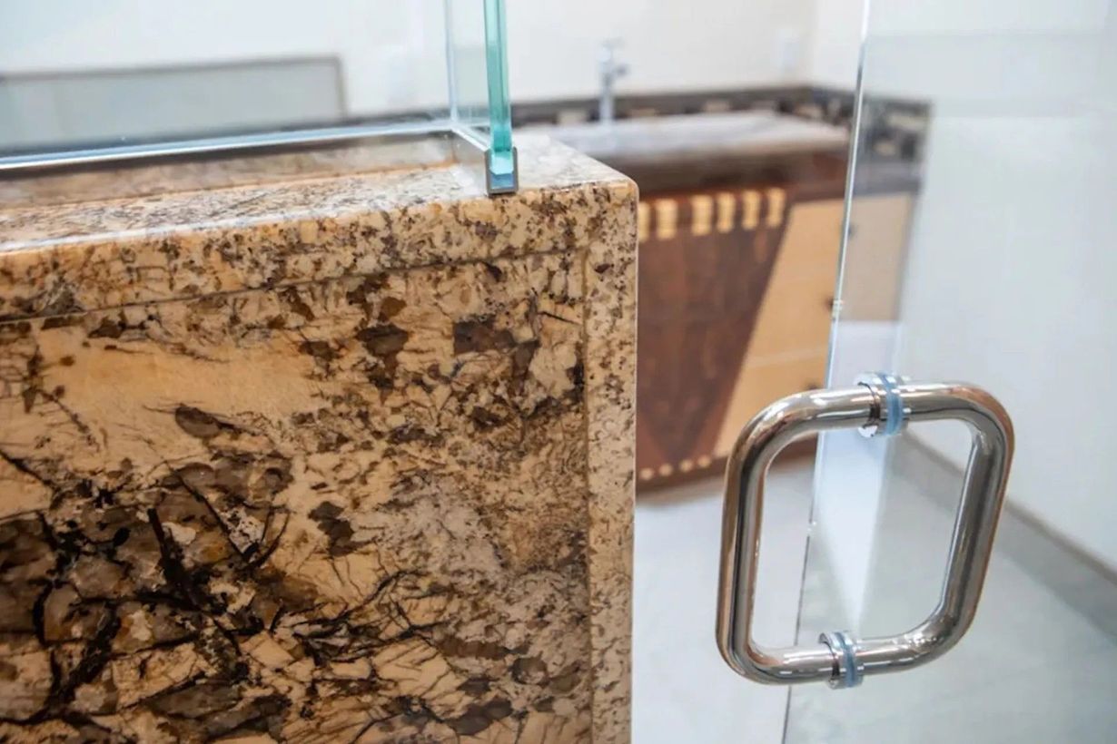 Granite countertop with a glass shower door and stainless steel handle.