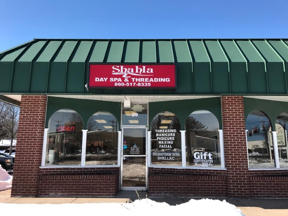A brick building with a green roof and a red sign that says day spa threading