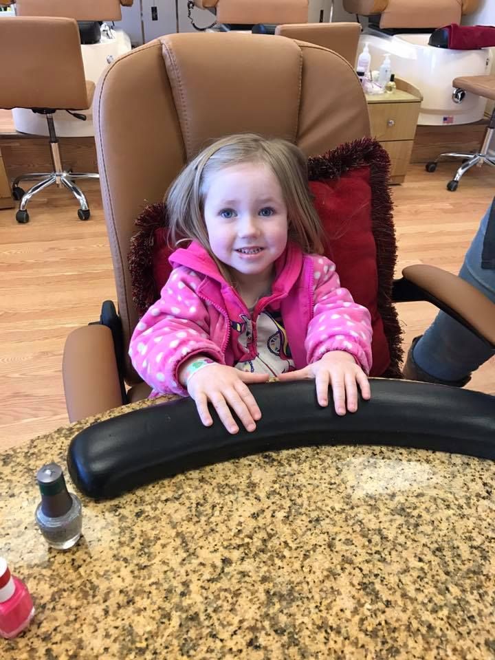 A little girl is sitting in a chair at a nail salon.