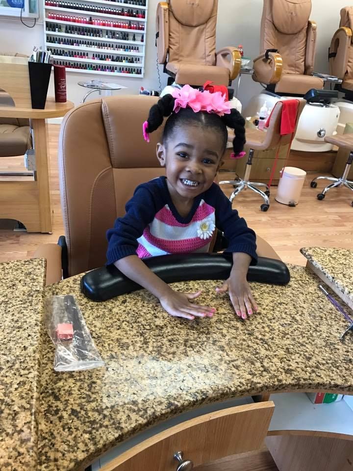 A little girl is sitting at a table in a nail salon.