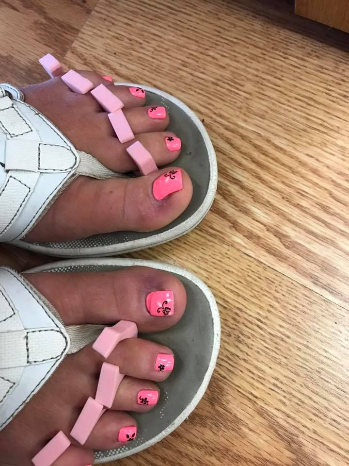 A woman 's feet with pink nails and white flip flops on a wooden floor.