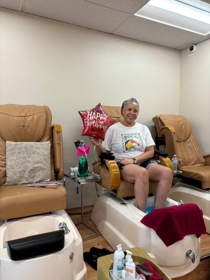 A woman is sitting in a chair in a nail salon holding a balloon.